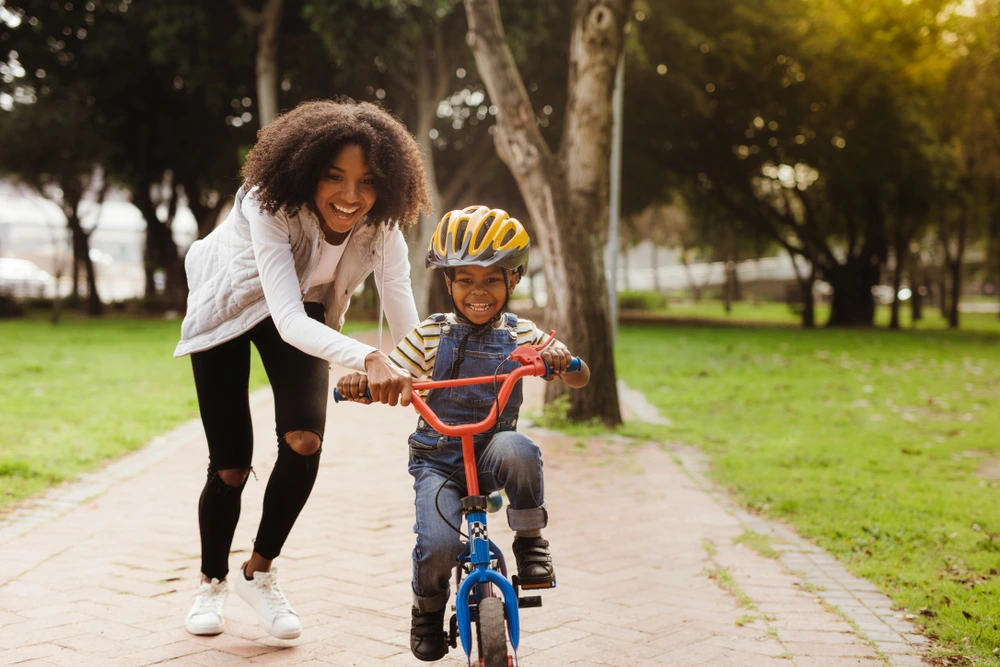 Mum helping her son ride a bike on the school holidays | Swoosh Finance