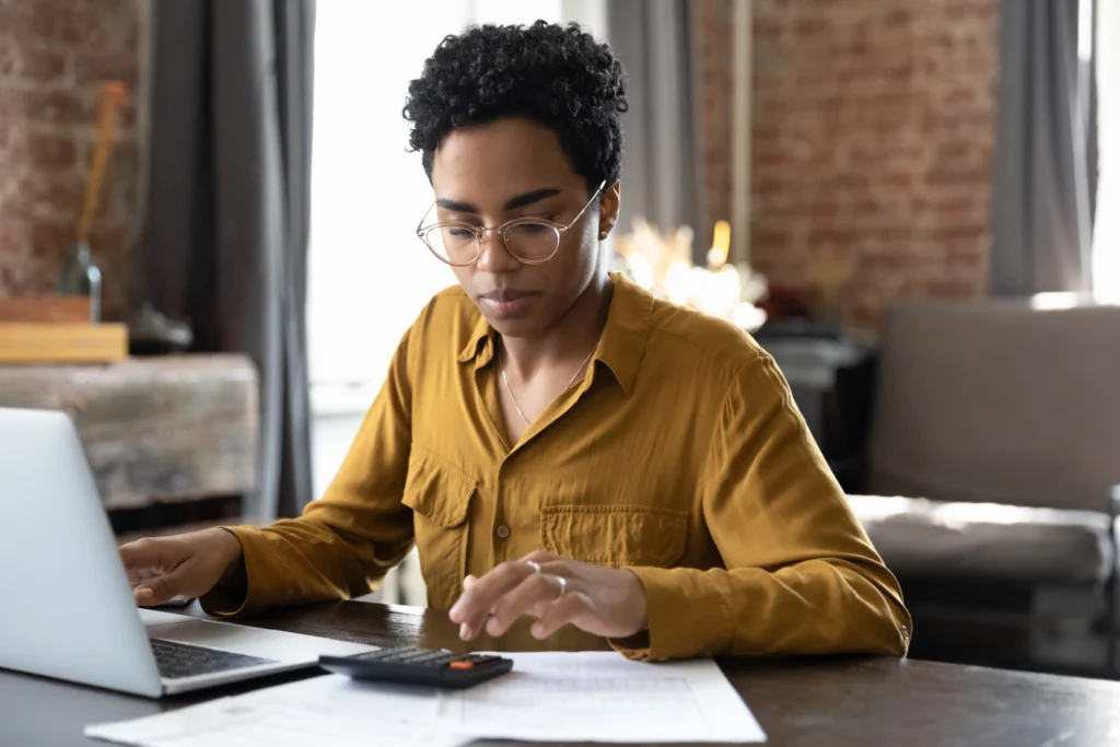 Woman with glasses uses her laptop and a calculator to make a household budget