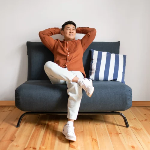 Smiling man sits with his arms behind his head on a couch after learning how to be a minimalist and save money